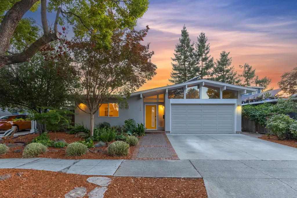 1186 Lyons Street at dusk, with a glazed clerestory gable above the garage and a yellow front door lit from within.