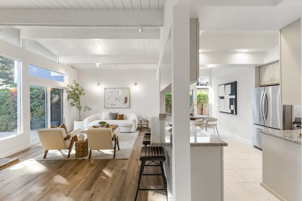 Looking from the kitchen through the living room to sliding glass, with a granite counter and bar stools in the foreground.
