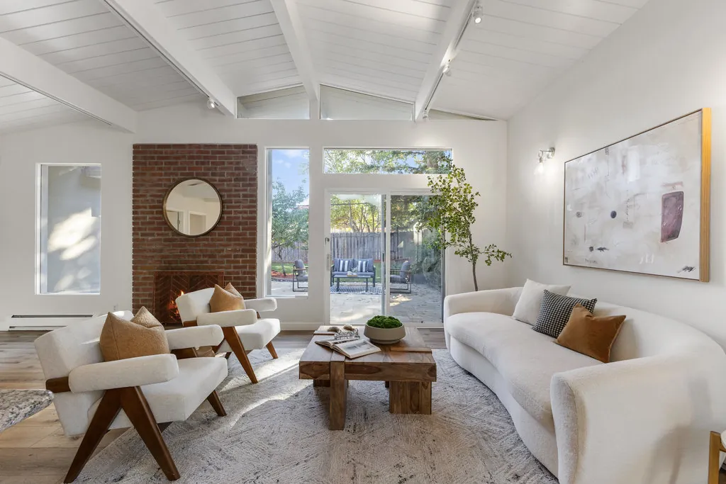 A cathedral ceiling of painted tongue-and-groove boards carried on exposed beams, above a living room with a brick fireplace.