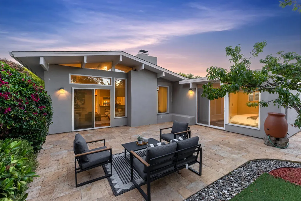 The rear patio at 1186 Lyons Street at dusk, travertine paving with the house lit behind sliding glass on two elevations.