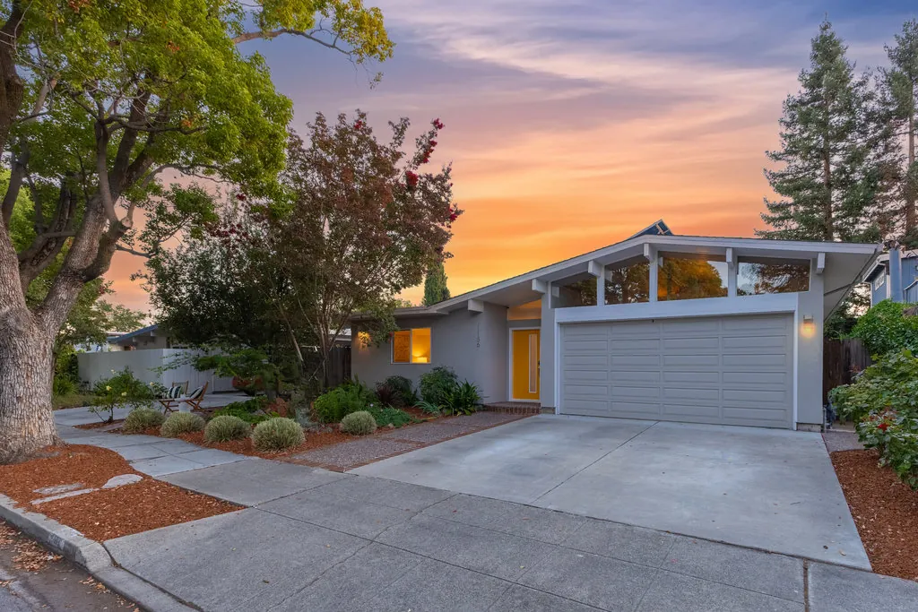 The full street elevation of 1186 Lyons Street at dusk, showing the driveway, the low roofline and the lit clerestory.