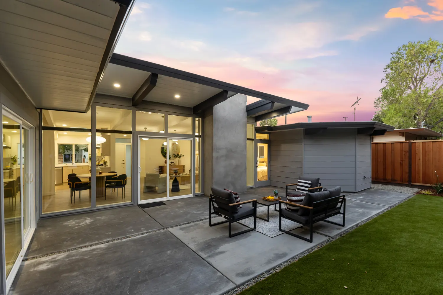 A dusk view across the patio into a lit dining room and kitchen, seen through sliding glass.