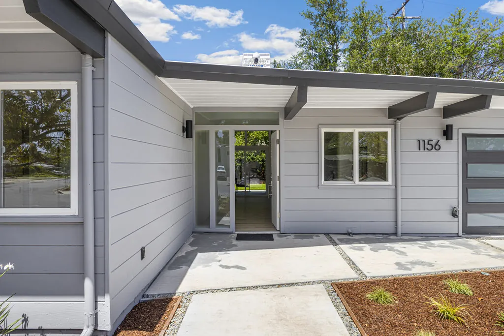 The entry elevation with the house number beside a front door with full-height sidelights, under a deep overhang carried on exposed beams.