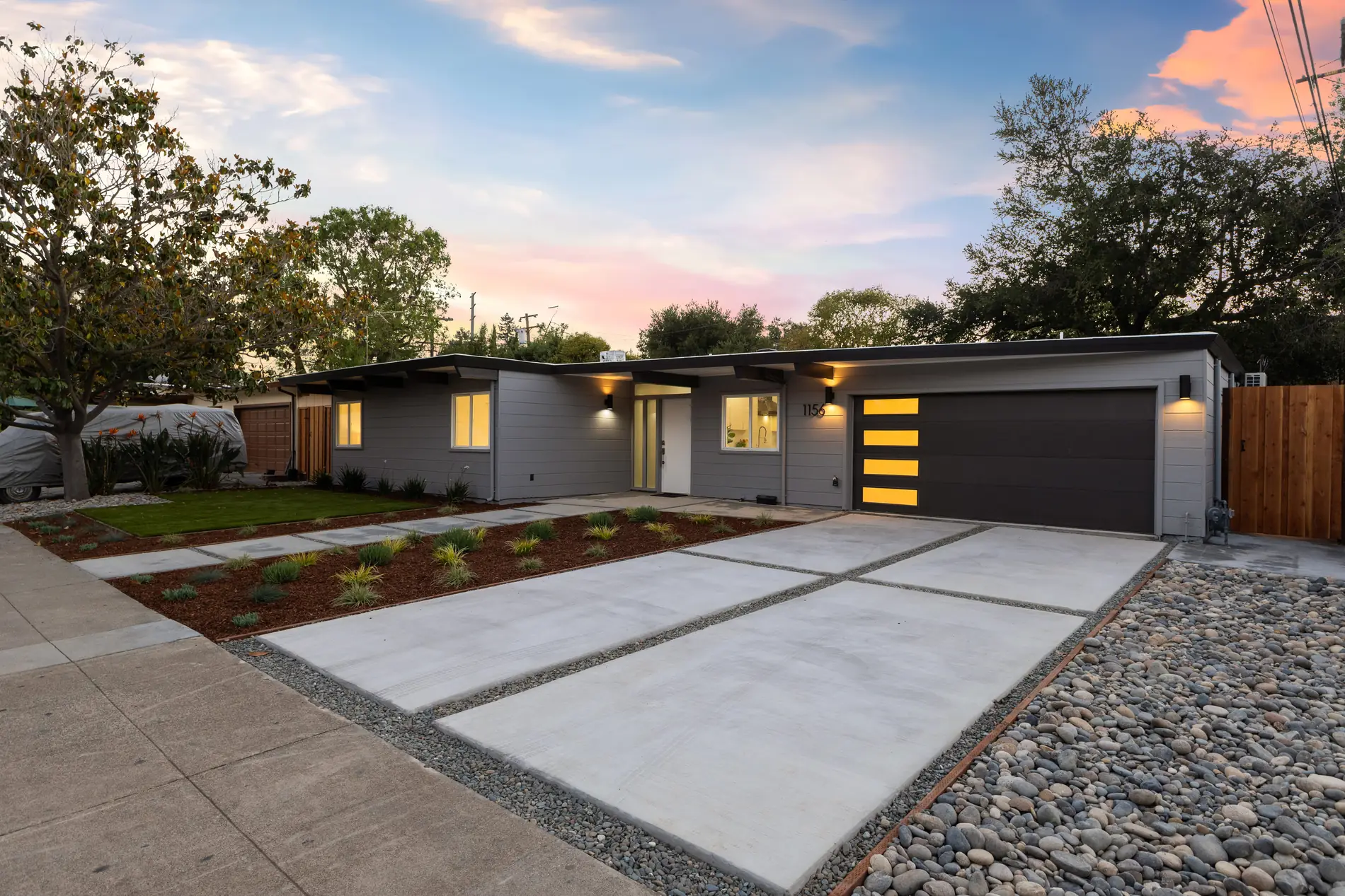 The same Atherwood Eichler at dusk, clerestory and garage glazing lit from inside beneath a low roofline.