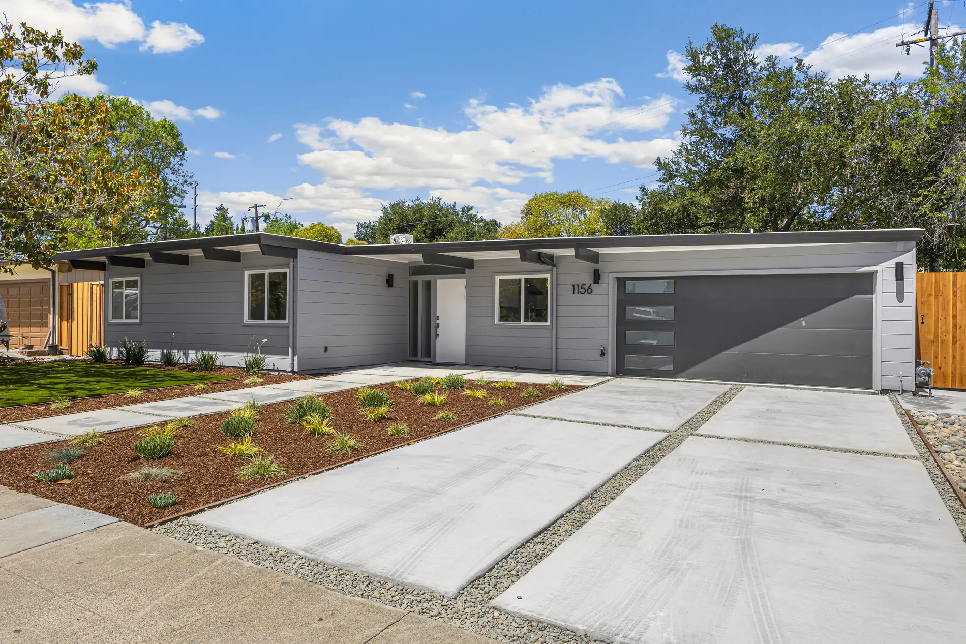 1156 Parkwood Way in daylight: a low-slope 1950 Eichler with grey board siding, exposed beam tails and drought planting.