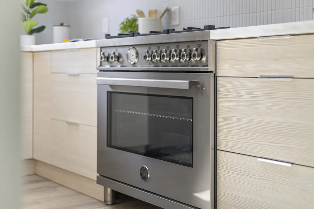 A kitchen with a stainless range set into pale custom cabinetry beneath a quartzite counter.