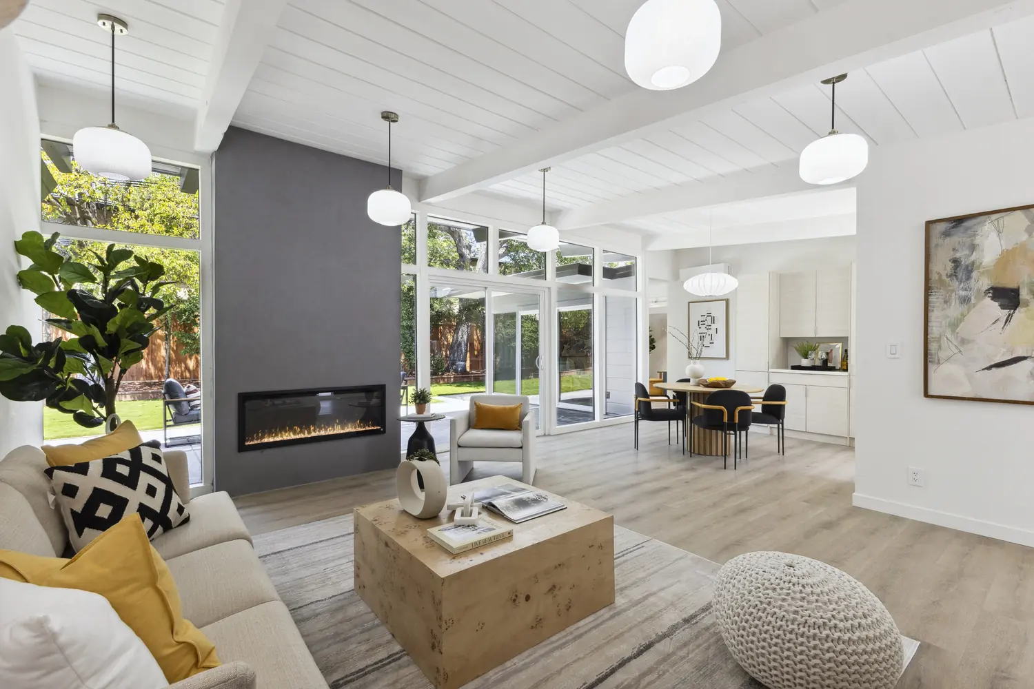 Living and dining under a continuous beamed ceiling, with sliding glass to the patio on two sides of the room.