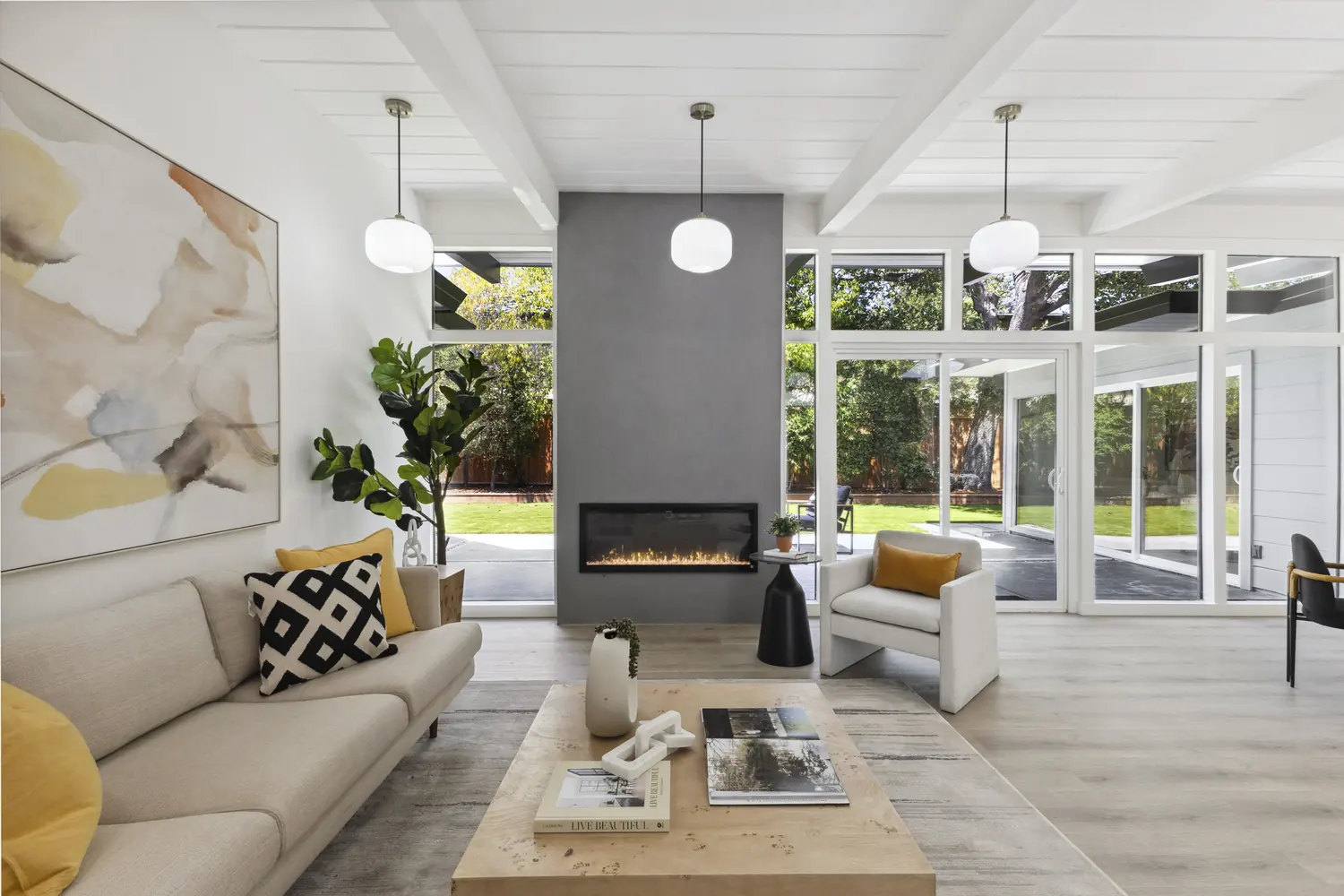 An Eichler living room with a linear fireplace between full-height glass walls opening to a garden.
