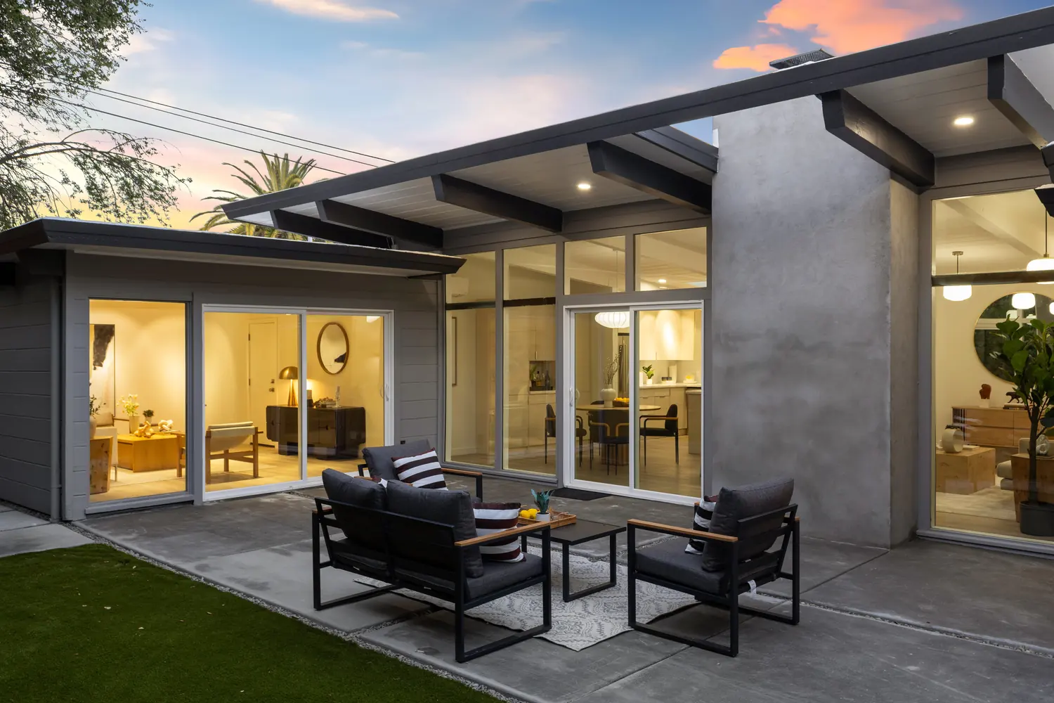 The covered rear terrace at dusk, warm interior light behind full-height glass.