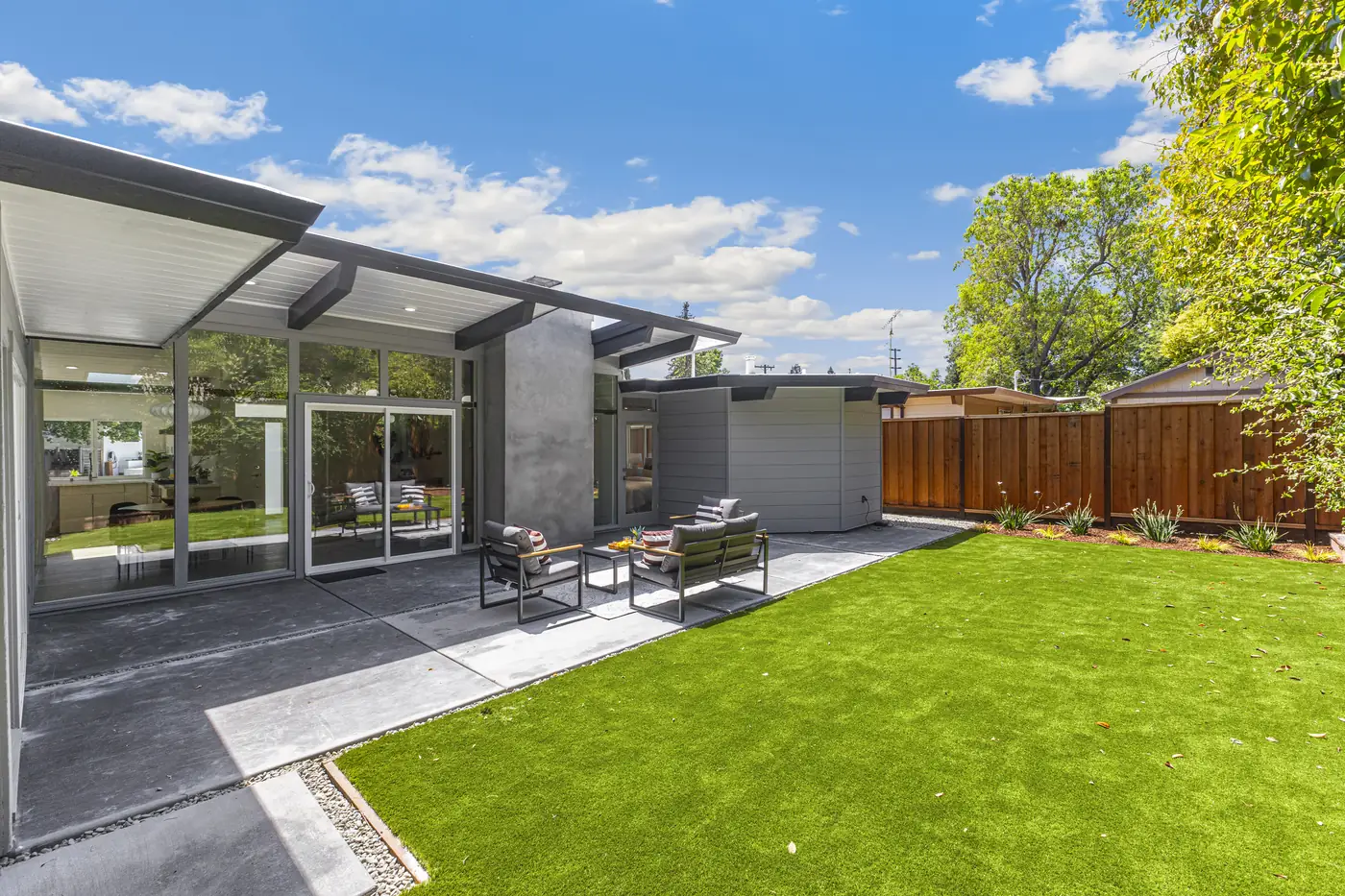 The rear elevation in daylight, with a deep roof overhang shading a concrete patio and a lawn beyond.