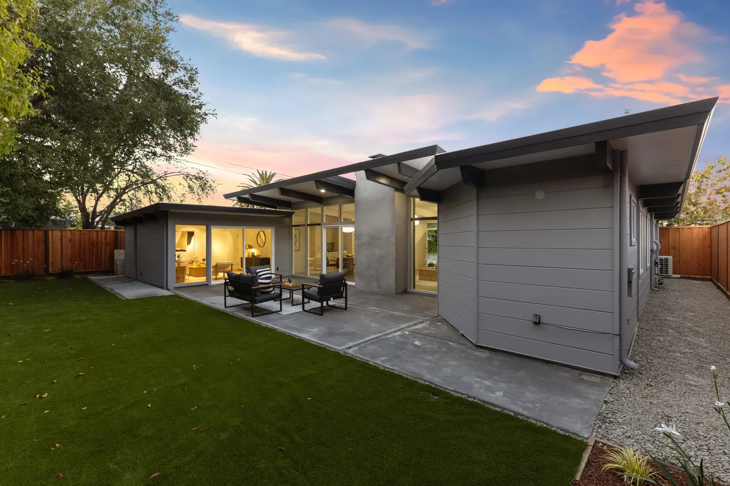 The full rear elevation of an Atherwood Eichler at dusk: the roof folding down over a patio, with the bedroom wing at one end and the living wing at the other.
