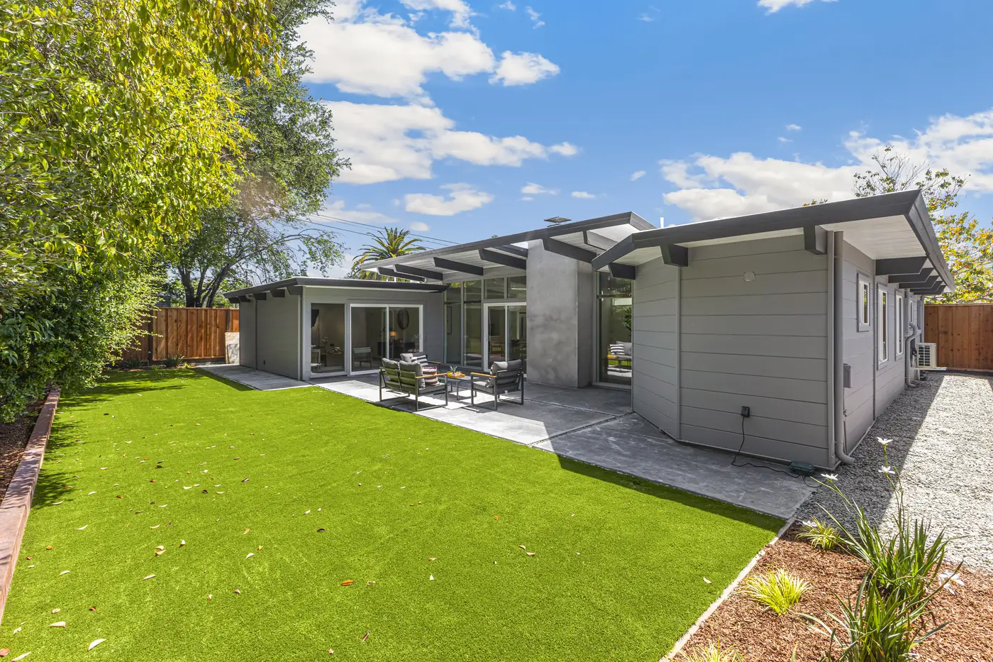 An Atherwood Eichler seen from the far corner of its lot, the L-shaped plan wrapping an open lawn behind full-height glass.