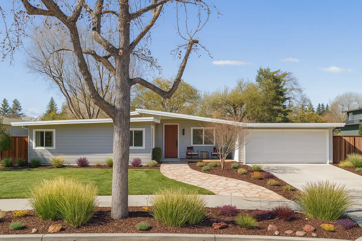 A single-storey mid-century house with a wide fascia and wood front door, behind a mature sycamore.